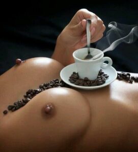 Beautiful Buxom Naked woman with bare breasts bosoms and perky nipples has coffee cup with some coffee beans on her chest and stirring the coffee in it
