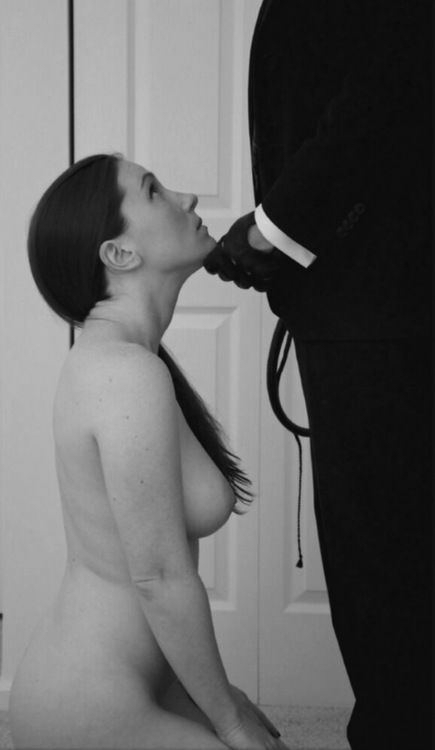 BDSM Submissive slave sitting at her Master's Sir's feet obediently and looking up to him and awaiting his instructions and orders in complete obedience whilst he lifts her chin up with his fingers